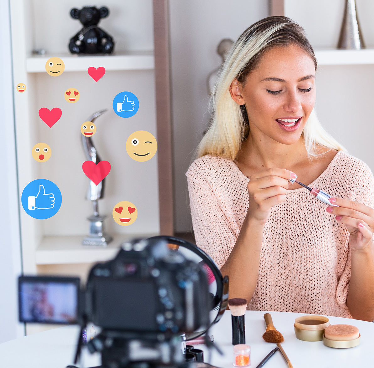 Woman filming herself putting on makeup. Emojis and heart icons floating around camera.