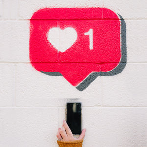 Woman holding phone up to wall with Instagram like icon spray painted on white wall